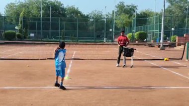 Delhi, Hindistan, 17 Şubat 2025 - Maha Open için kil tenis kortunda antrenörlük yapan genç tenisçiler, yaklaşan turnuva için küçük tenis oyuncuları antrenman yapıyor