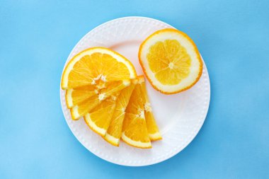 Portakal, sulu, olgun portakal dilimleri beyaz bir tabağa konur. Yapraklar fırıldak şeklindedir. Güzel mavi arkaplan.