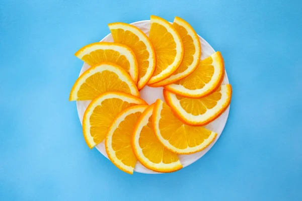 Orange - slices of juicy, ripe orange laid on a white plate. The petals form the shape of a pinwheel. Beautiful blue background.