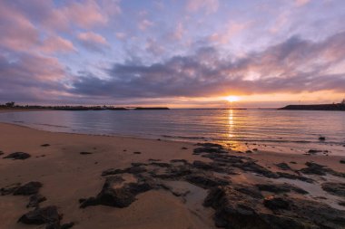 Fuerteventura, Coralejo plajı. Ön planda, sahilde kayalar ve arka planda, güneş doğarken..