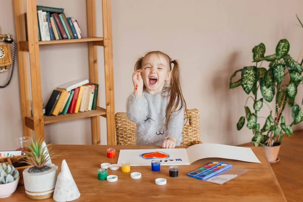 Little happy cute girl draws with paints at the table in the living room. Happy childhood concept. High quality photo