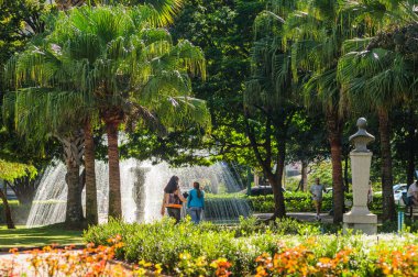 27 Haziran 2008 'de Liberty Square, Belo Horizonte, MG, Brezilya' da yürüyen insanlar. Güneşli bir günde çevrede çiçekler, ağaçlar ve binaların olduğu şehir manzarası.