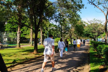27 Haziran 2008 'de Liberty Square, Belo Horizonte, MG, Brezilya' da yürüyen insanlar. Güneşli bir günde çevrede çiçekler, ağaçlar ve binaların olduğu şehir manzarası.