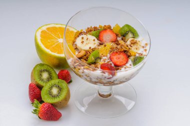 Çilekli yoğurt, üzüm, muz, papaya, portakal, beyaz arka planda cam bir kasede kivi gibi meyveler. Sağlıklı yemek..