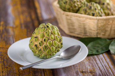 Beyaz tepside, paslanmaz çelik kaşıkla yenmeye hazır elma şekeri. Diğer elma şekerlerine ek olarak eski sarı ahşap bir masada bulanık bir arka planda bir sepet içinde.