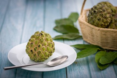 Beyaz tepside, paslanmaz çelik kaşıkla yenmeye hazır elma şekeri. Mavi ahşap bir masada bulanık bir arka planda sepetteki diğer elma şekerlerine ek olarak.