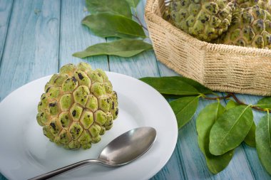 Beyaz tepside, paslanmaz çelik kaşıkla yenmeye hazır elma şekeri. Mavi ahşap bir masada bulanık bir arka planda sepetteki diğer elma şekerlerine ek olarak.