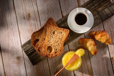 Cam kavanozda tereyağı, tahta spatula ve ahşap masada dilimlenmiş ekmek..