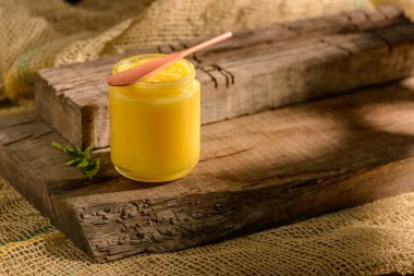 Ghee butter in glass jar with wooden spatula on wood. clipart