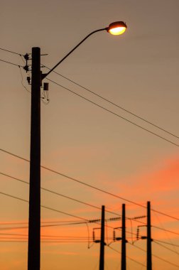 Turuncu gün batımı arkaplanlı elektrik direkleri.