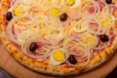 Haşlanmış yumurtalı Portekiz pizzası, ahşap tahtada soğan ve zeytin ve arka planda sebze..