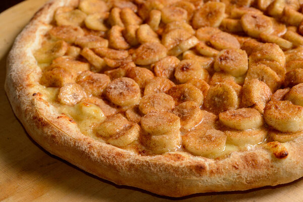 Banana pizza with sugar and cinnamon on wooden board. Brazilian sweet pizza.