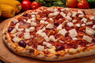 Palmiyeli pizzanın kalbi ahşap bir tahtanın üzerinde pastırma ve arka planda sebzeler.
