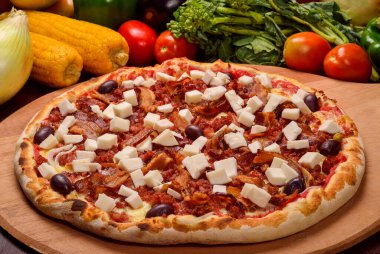 Palmiyeli pizzanın kalbi ahşap bir tahtanın üzerinde pastırma ve arka planda sebzeler.