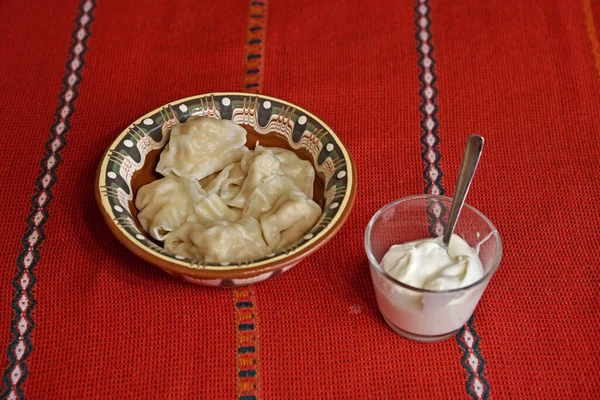 Bir tabak hamur köftesi ve bir bardak ekşi krema kırmızı masa örtüsünün üstünde..