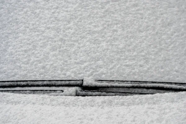 Snow covered windshield with wiper blades. Frozen snow on car in cold winter morning. Concept of driving in winter time with snow on road. Winter season