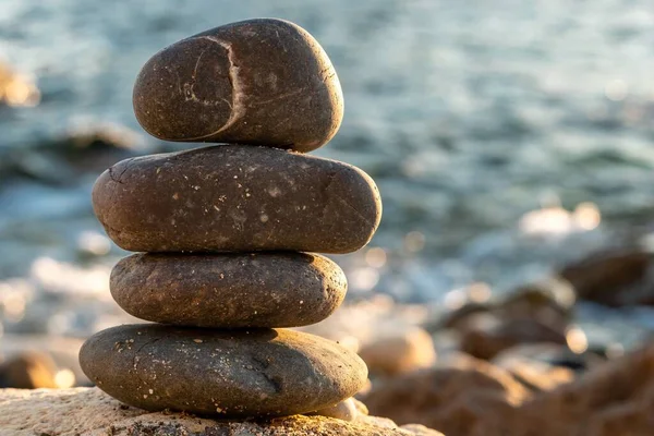 Balanced pebble pyramid silhouette on the beach. Abstract warm sunset bokeh with Sea on the background. Zen stones on the sea beach, meditation, spa, harmony, calmness, balance concept Selective focus