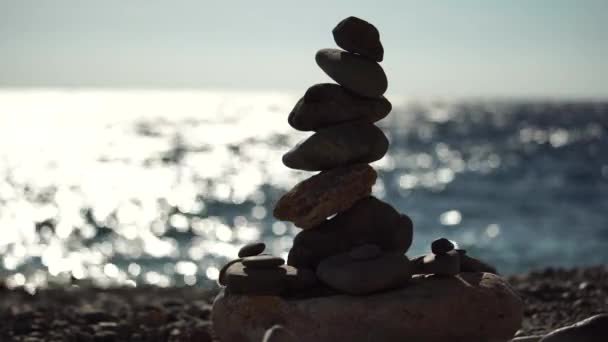 Vyvážená oblázková pyramida na pláži za slunečného dne. Abstraktní mořský bokeh na pozadí. Selektivní soustředění. Zenové kameny na mořské pláži, meditace, lázně, harmonie, klid, rovnováha koncept