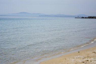Ufukta uzak dağları olan boş bir deniz kıyısı. Sakin, şeffaf suyu olan kumsal..