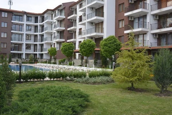 The courtyard of apartment building with balconies, covered with manicured lawn and trimmed trees and bushes and a swimming pool — Stock Photo, Image