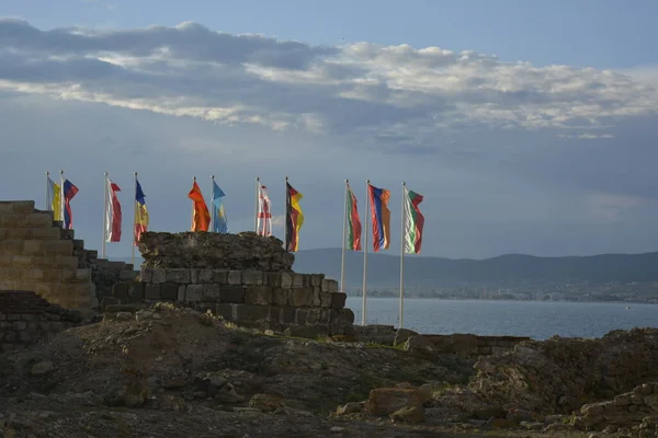 Rüzgarda sallanan birçok ülkenin ulusal bayrakları. Eski kalıntılar. Arka planda deniz limanı.