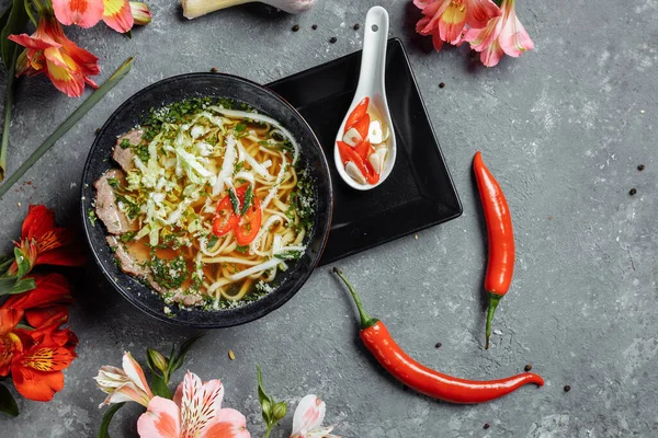 Asian cuisine, Beef soup fo in a black plate on a dark background. Soup Fo with Spicy beef broth, beef tenderloin, udon noodles, chili paste, Beijing cabbage, chili pepper, cilantro, Picked sauce — Stock Image Asian Cuisine Beef Soup Black Plate Dark Background Soup Spicy Stock Image