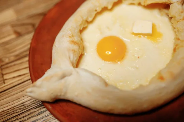 Vue de dessus sur le traditionnel Adjarian Khachapuri - tarte ouverte au four avec du suluguni au fromage salé fondu et du jaune d'oeuf sur un plateau en bois. Nourriture géorgienne traditionnelle — Photo