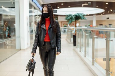 Siyah maskeli bir kız alışveriş merkezi boyunca yürüyor. Koronavirüs salgını. Maskeli bir kadın alışveriş merkezinde duruyor. Koruyucu maskeli bir kız alışveriş merkezinde alışveriş yapıyor..