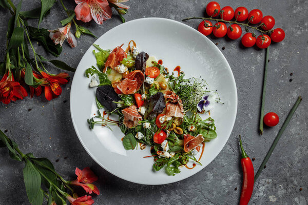 Fresh salad with ham and pear on a dark gray background. jamon salad, salad mix, spinach, pear, cherry tomatoes, Dor Blue, capers and vinegar dressing Bianco.