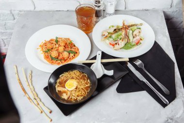 Lokantada bir masada üç çeşit menü. Tavuk ve yumurtalı ramen, taze sezar salatası ve makarna..