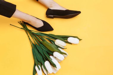 Güzel kadın bacakları şık siyah düz ayakkabılar giyer. Sarı arka planda siyah sandaletler.