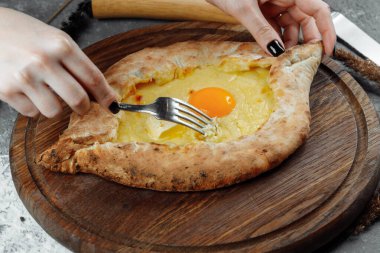Bir restoranda bir tabakta Adjarian Khachapuri 'de yumurta peynirini çatal ve bıçakla karıştıran kadın eli. Gürcistan ulusal yemeği