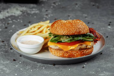 Peynirli hindi burger, marul, domates ve taze salatalık. Gri bir zemin üzerinde hindili pirzola ve patates kızartması sosu ve salata..