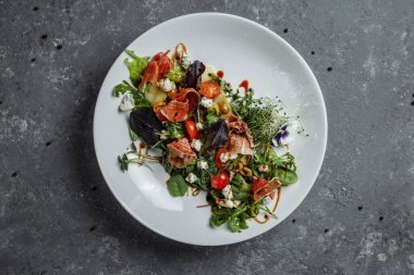 Koyu gri arka planda armut ve jambonlu taze salata. Jamon salatası, salata karışımı, ıspanak, armut, kiraz domates, Dor Blue, kapari ve sirke sosu Bianco.