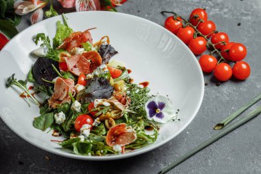 Jambonlu salata ve koyu gri arka planda armut. Jamon salatası, salata karışımı, ıspanak, armut, kiraz domates, Dor Blue, kapari ve sirke sosu Bianco