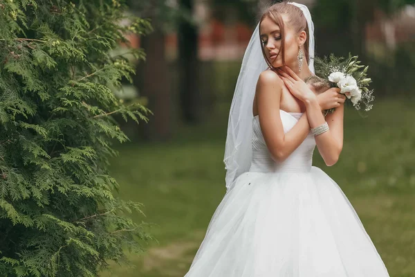 Pengantin wanita cantik dengan gaun pengantin megah berpose di antara tanaman hijau di jalan. Konsep pengantin untuk gaun iklan — Stok Foto