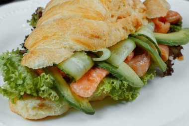 Kırmızı balıklı kruvasan sandviçi, avokado, taze sebzeler ve siyah taş zemin üzerinde roka. Sağlıklı gıda konsepti.