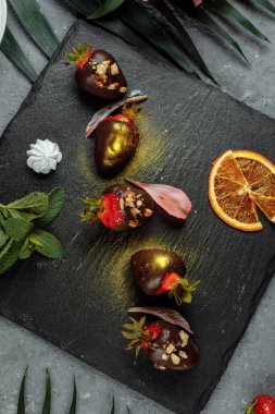 Gri dekoratif arka planda taze çikolata kaplı çilekler. Yaz mevsimi menüsünün reklamını yapma kavramı.