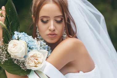 Muhteşem gelinlikli güzel gelin sokakta yeşillikler arasında poz veriyor. Gelinlik reklamları için gelinlik konsepti