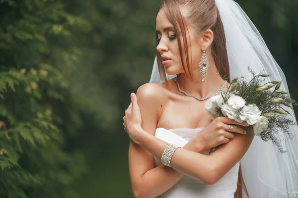 Pengantin wanita cantik dengan gaun pengantin megah berpose di antara tanaman hijau di jalan. Konsep pengantin untuk gaun iklan — Stok Foto