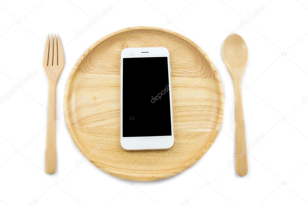 Top view smartphone on wooden dish with spon and fork on white background, concept Eating technology