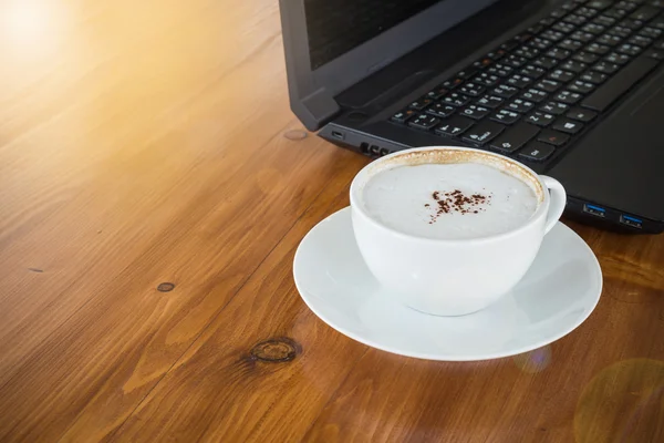 Art Latte Coffee in a white cup on wooden table with computer laptop background — Stock Photo, Image