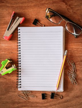 Üstten Görünüm kalem, gözlük, ATAÇ ile boş not defteri çalışma alanından arka plan şeritler üzerinde ahşap masa. Metin için yer kopyalayın
