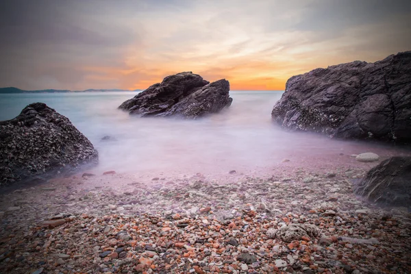 Zachte golven van de Oceaan in zonsondergang met stenen op het strand voorgrond — Stockfoto