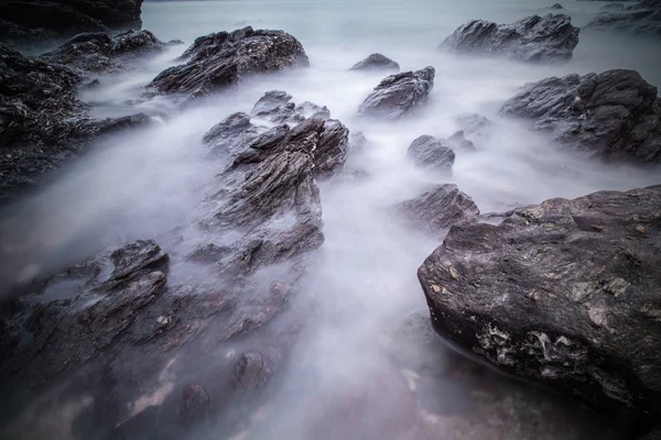 Gün batımında kumsal arka planında taşlarla okyanusun yumuşak dalgaları — Stok fotoğraf