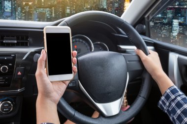 Gece şehir arka planına sahip bir arabada dokunmatik ekranlı akıllı telefon ve direksiyon kullanan genç bir kadın sürücü.