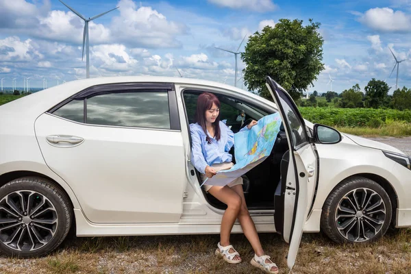 woman in a car looking at a map to reach the holiday destination with blue sky and wind turbines background