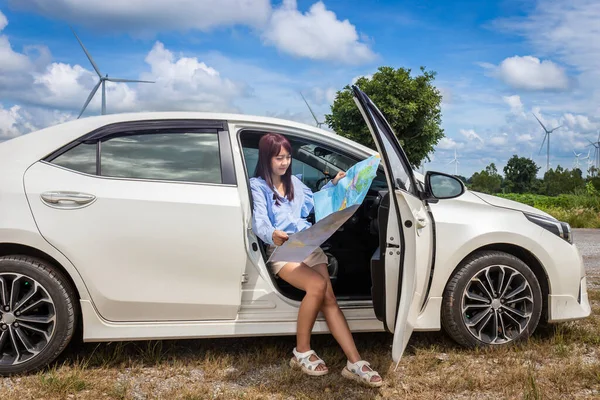 woman in a car looking at a map to reach the holiday destination with blue sky and wind turbines background