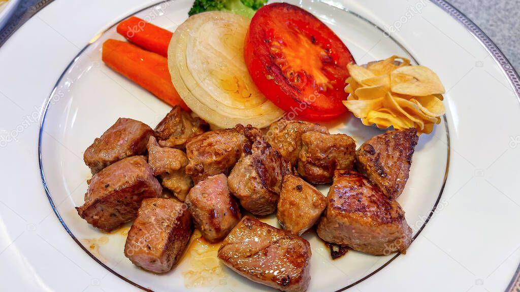 Beef steak Cut into squares in a plate with tomatoes, onions, carrots on the table.