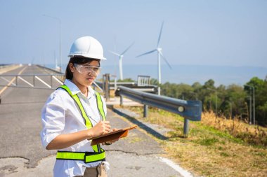 Asyalı kadın mühendisler dışarıdaki elektrik santralinin enerji türbinlerini kontrol edip teslim ediyorlar.